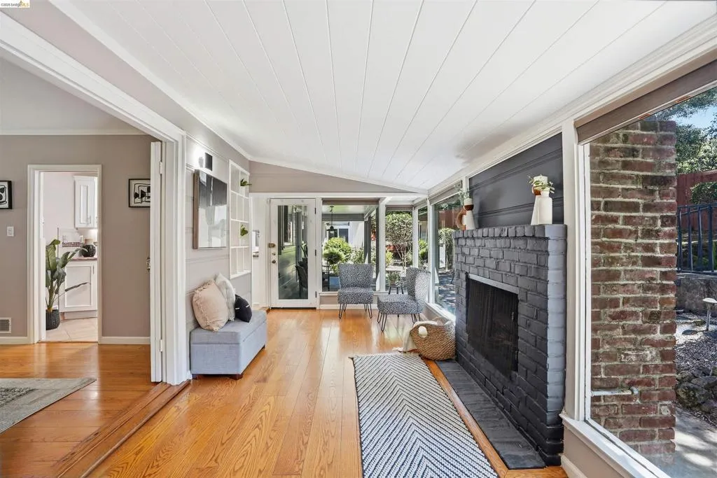 Bright living area featuring a painted brick fireplace, a vaulted ceiling with white planking, and wood-finish flooring