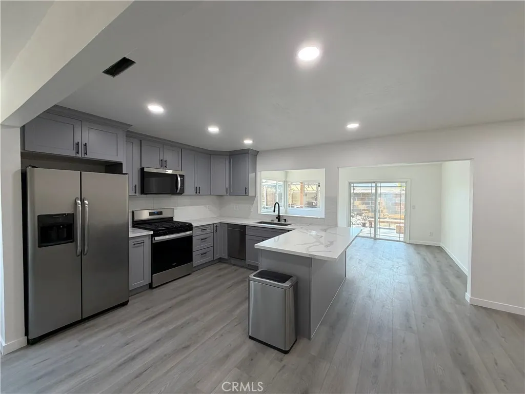 New kitchen featuring custom cabinetry, high-end stainless steel appliances, a spacious quartz center island, new flooring, modern recessed lighting, and a seamless transition to the adjoining dining area.
