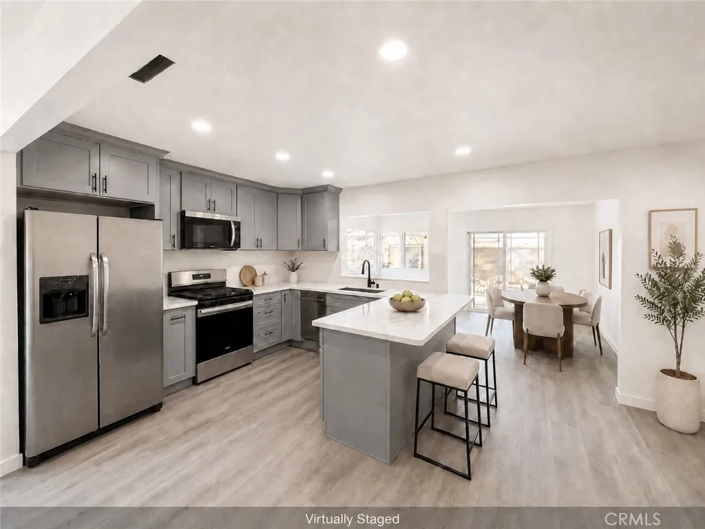 New kitchen with new cabinetry, stainless steel appliances, center  quartz island, new recessed lighting, and adjoining dining area. Virtually staged.