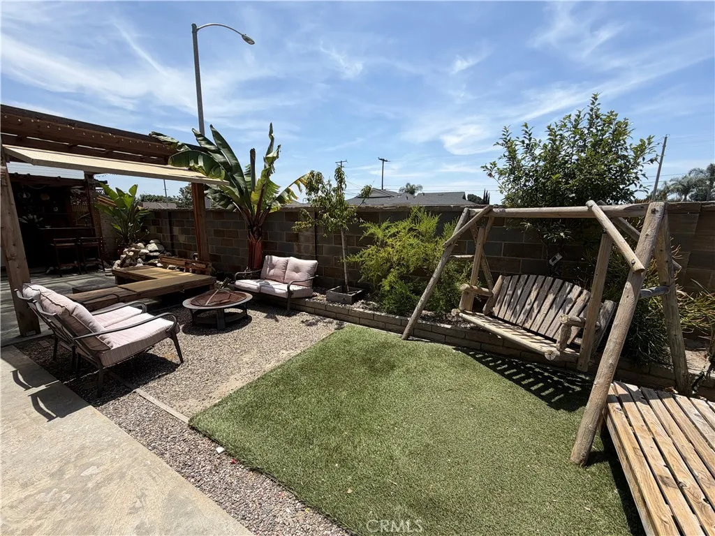 Backyard with artificial turf, covered patio area, seating space, wood swing, and low-maintenance landscaping.