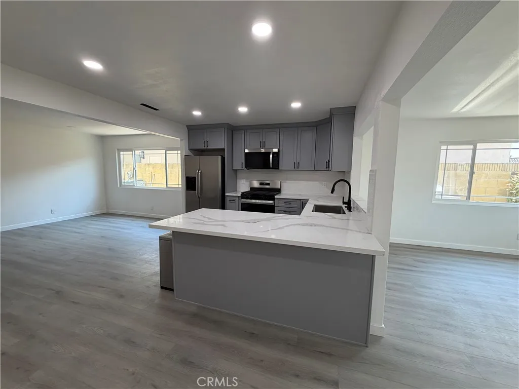Open-concept kitchen with quartz-style island, gray cabinetry, recessed lighting, and adjoining living and dining areas.