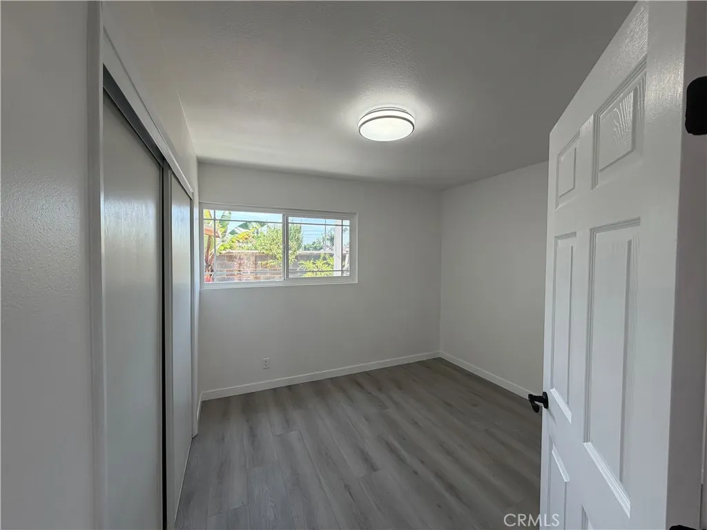 Middle bedroom with updated flooring, neutral paint, closet doors, modern light fixture, and natural light.