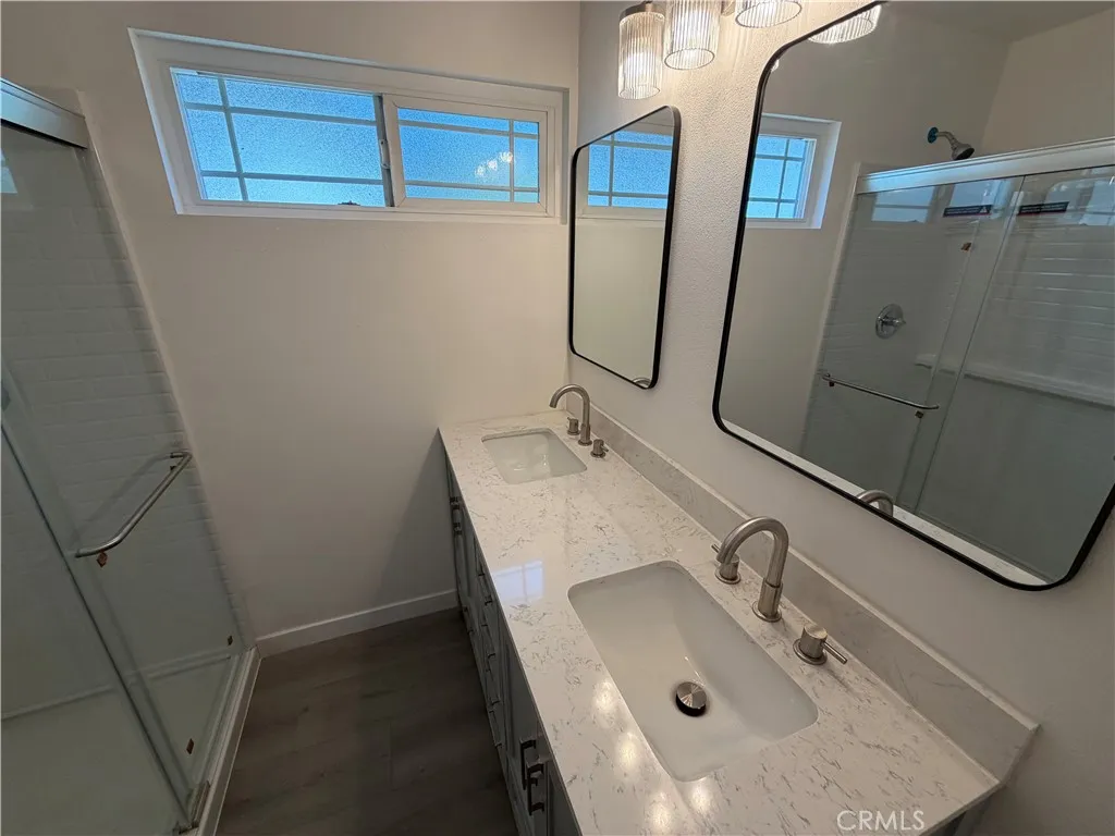 Primary bathroom with new flooring, new quartz-style countertops, dual sinks, new shower enclosure, and modern fixtures.