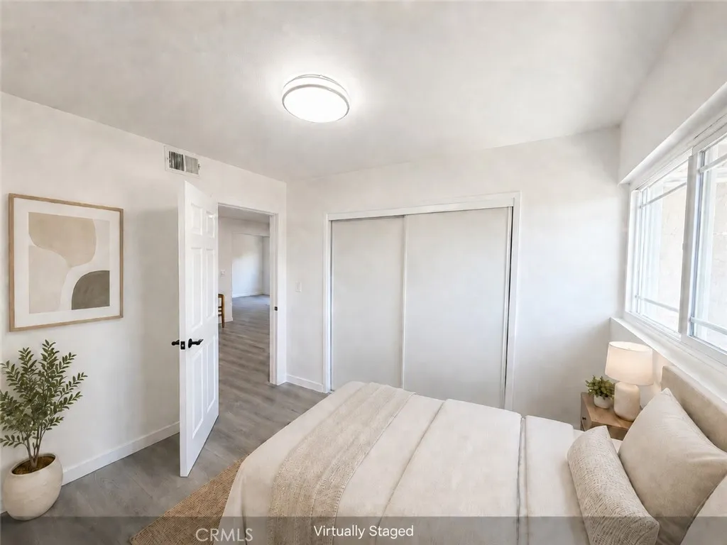 Virtually staged bedroom with wide-plank flooring, new door, closet, updated light fixture, and large window for natural light.