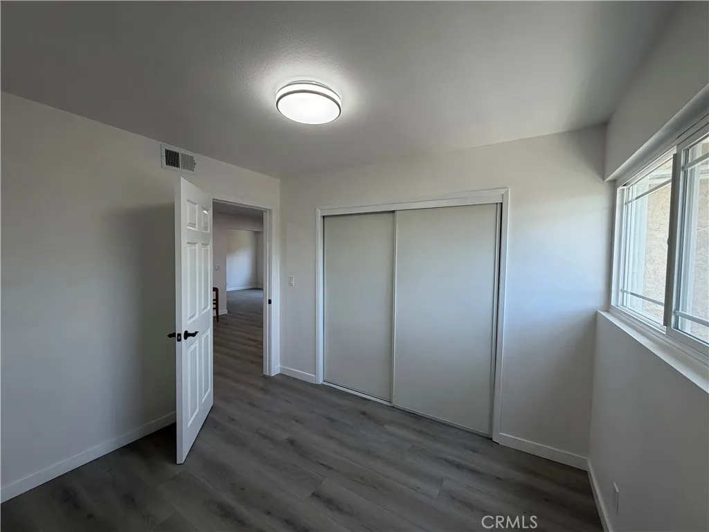  bedroom with wide-plank flooring, closet, updated light fixture, and large window for natural light.