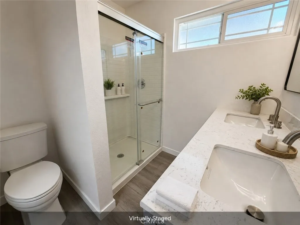 Virtually staged primary bathroom with new flooring, new quartz-style countertops, dual sinks, new shower enclosure, and modern fixtures.