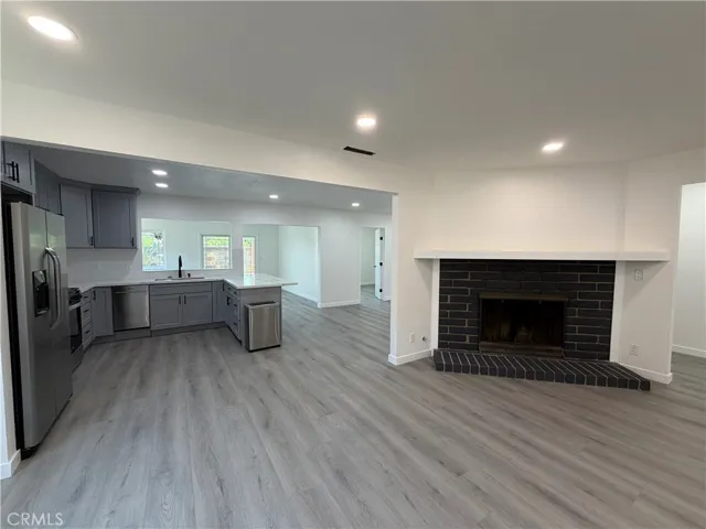Living room with new recessed lighting, fireplace, new flooring, and open flow to the kitchen.