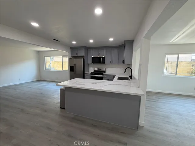 Open-concept kitchen with quartz-style island, gray cabinetry, recessed lighting, and adjoining living and dining areas.