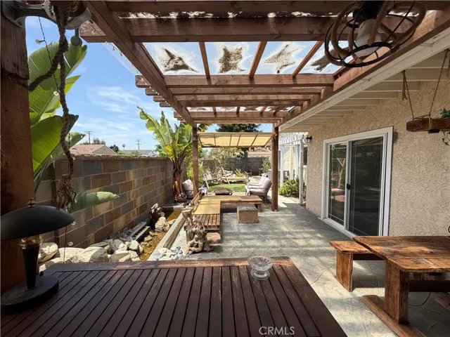 Backyard patio with wood pergola, sliding door access from dining room and south bedroom, hardscape area, and mature landscaping.
