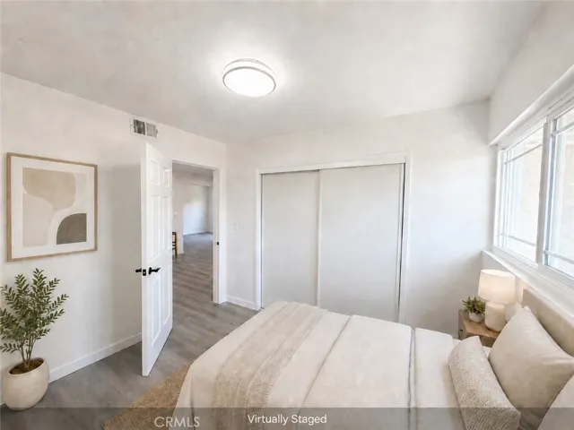 Virtually staged bedroom with wide-plank flooring, new door, closet, updated light fixture, and large window for natural light.