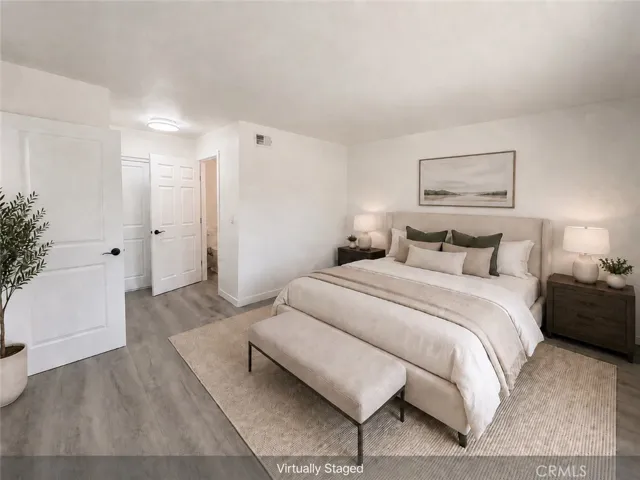 Virtually staged primary bedroom with wide-plank flooring, updated doors, neutral paint, and access to the primary bathroom.