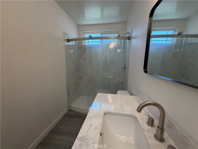 secondary bathroom featuring a quartz-topped vanity, contemporary mirror, modern fixtures, and a newly installed shower with a glass enclosure.