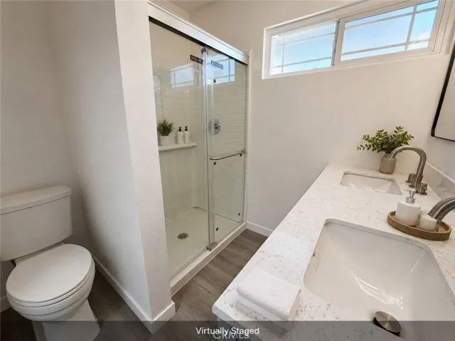 Virtually staged primary bathroom with new flooring, new quartz-style countertops, dual sinks, new shower enclosure, and modern fixtures.