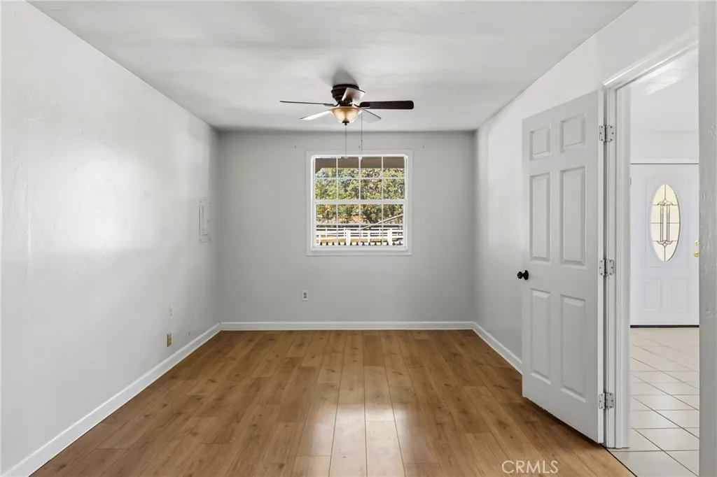 Guest House Bedroom – Comfortable bedroom with wood laminate flooring, a ceiling fan, and a large window providing natural light and outdoor views.