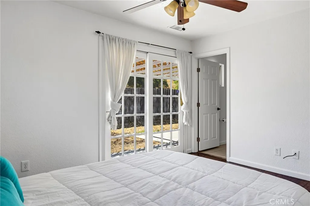 Primary Bedroom – Spacious primary bedroom featuring wood laminate flooring, a ceiling fan and sliding glass doors that open directly to the backyard patio, allowing for abundant natural light and indoor-outdoor access.