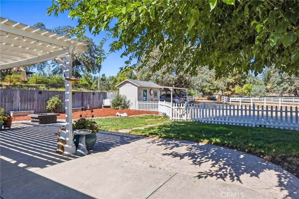 Front Patio View – Enjoy peaceful views of the landscaped yard, mature shade trees and charming fenced grounds from the pergola-covered front patio.