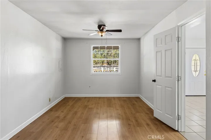 Guest House Bedroom – Comfortable bedroom with wood laminate flooring, a ceiling fan, and a large window providing natural light and outdoor views.