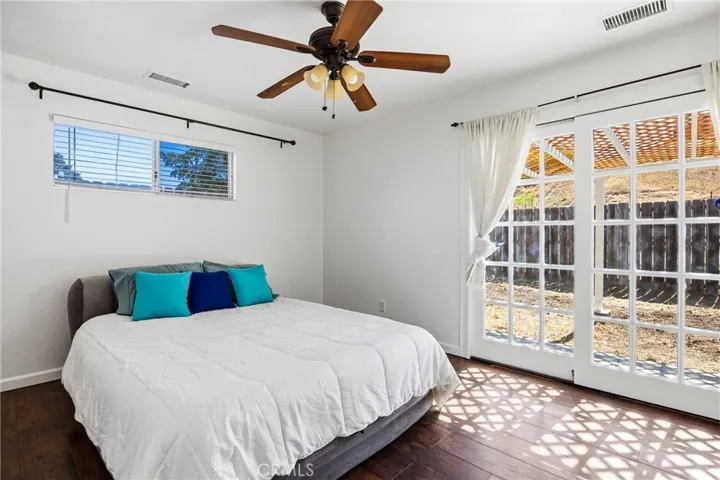 Primary Bedroom – Bright and inviting primary bedroom featuring window sliding doors to the backyard, abundant natural light, and warm wood laminate flooring.