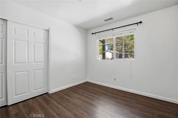 Bedroom – Comfortable bedroom featuring wood laminate flooring, a ceiling fan, sliding closet doors, and natural light from a large window.