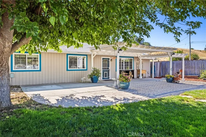 Front Exterior – Welcoming front exterior set beneath a mature shade tree, creating a picturesque park-like setting. A spacious pergola-covered patio, lawn, and attractive landscaping enhance the home's outdoor living space.