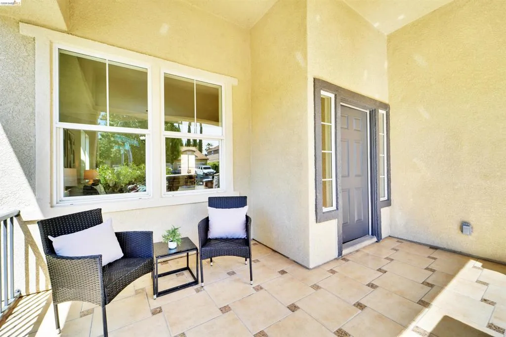 Covered front porch featuring a paneled entry door with sidelights, a large white-framed window, and patterned tile flooring