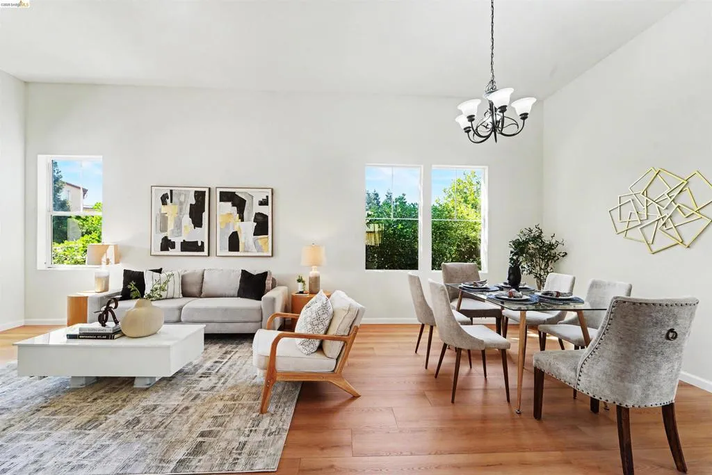Open-concept living and dining area featuring high ceilings, wood-finish flooring, multiple windows, and a classic chandelier