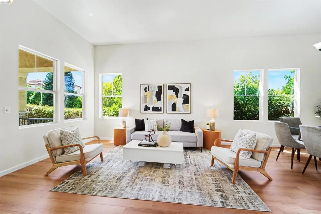 Spacious living area featuring light wood-finish flooring, abundant natural light from multiple windows, and a neutral color palette
