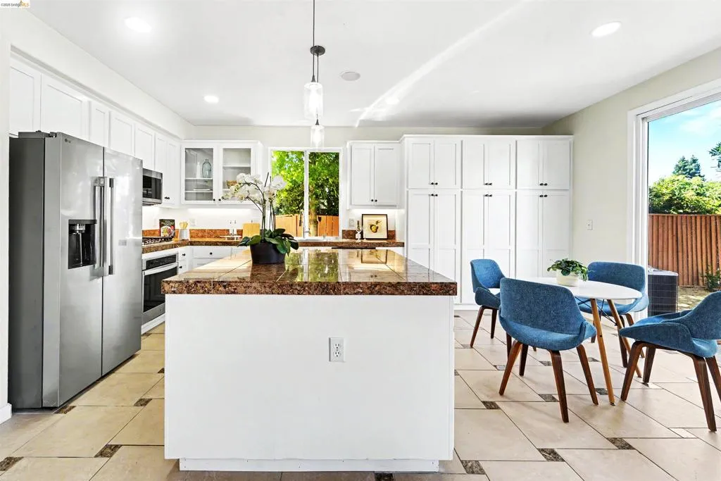 Kitchen featuring an island with a speckled countertop, white cabinetry, integrated stainless steel appliances, and tile flooring