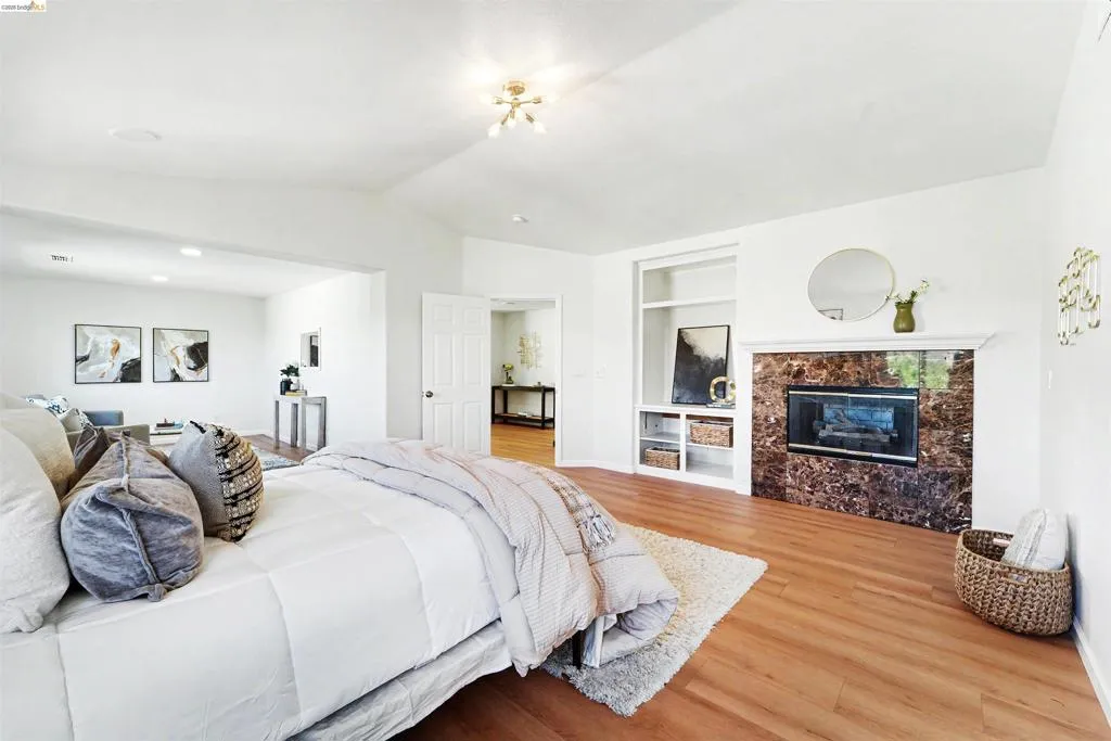 Spacious room featuring wood-finish flooring, a vaulted ceiling, and a fireplace with a stone surround