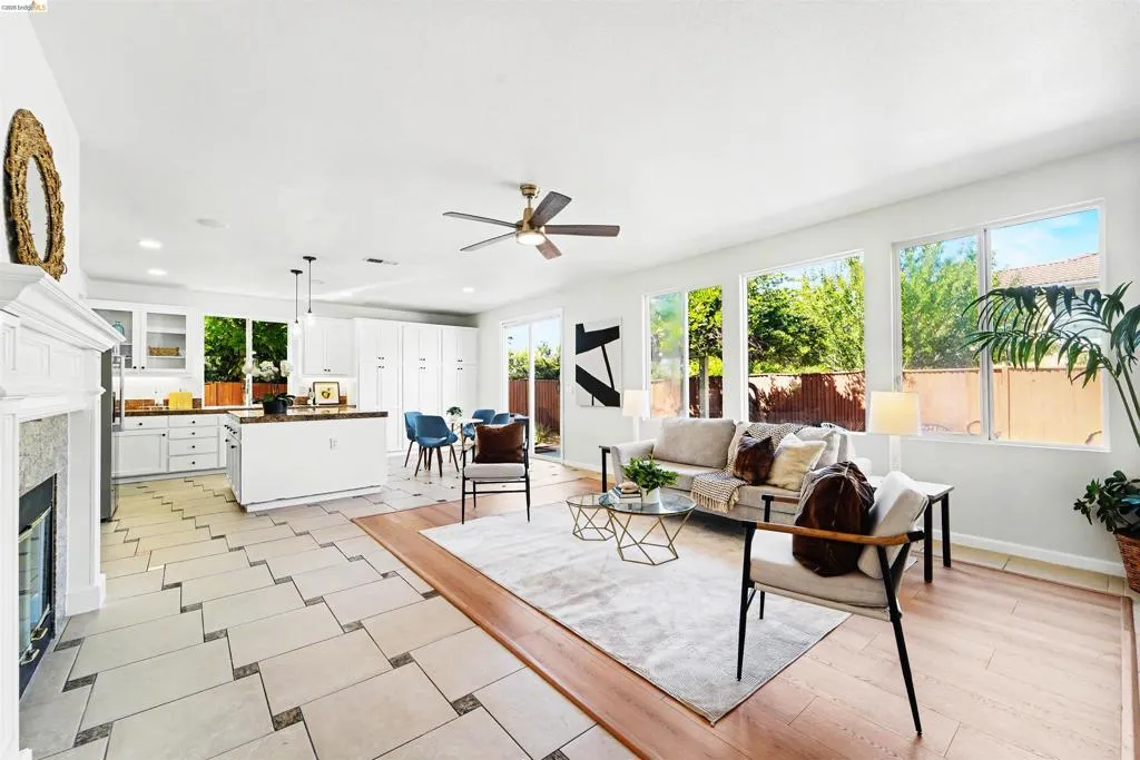 Open-concept living space featuring a fireplace with a white mantel, an island kitchen with white cabinetry, and wood-finish flooring