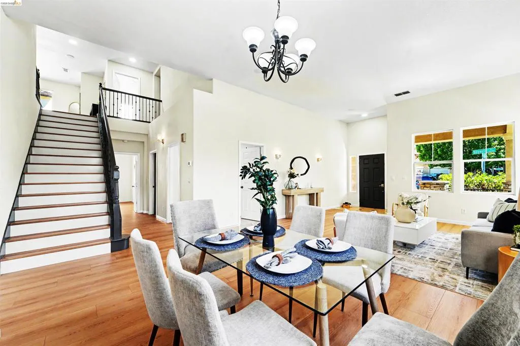 Open-concept living area with wood-finish flooring, a two-story staircase featuring dark wood newel posts and railings, and recessed lighting