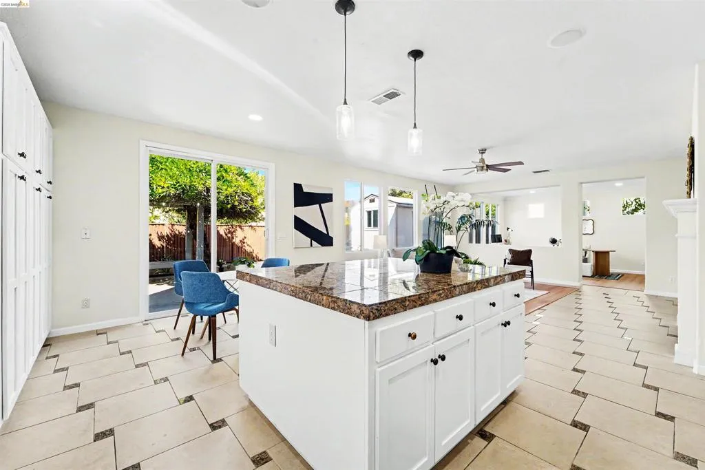 Kitchen island with a granite countertop, white cabinetry, and pendant lighting