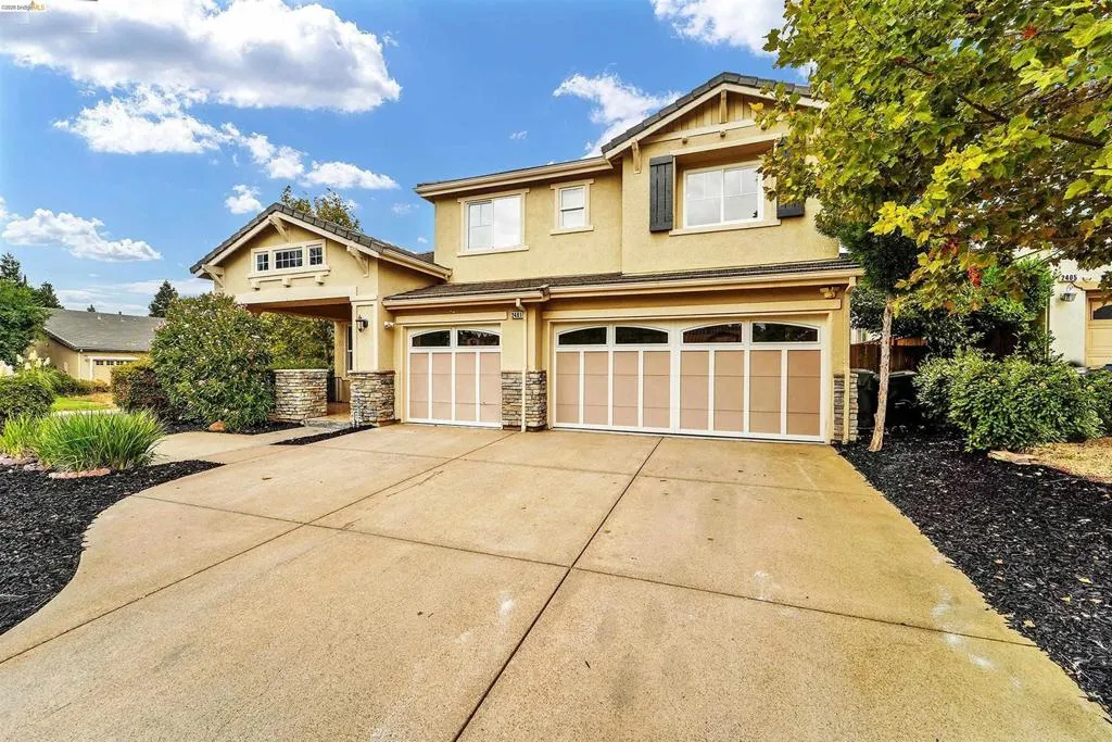 Two-story residence featuring a stucco exterior, a two-car garage with paneling and upper windows, and a covered entry with stone-wrapped columns