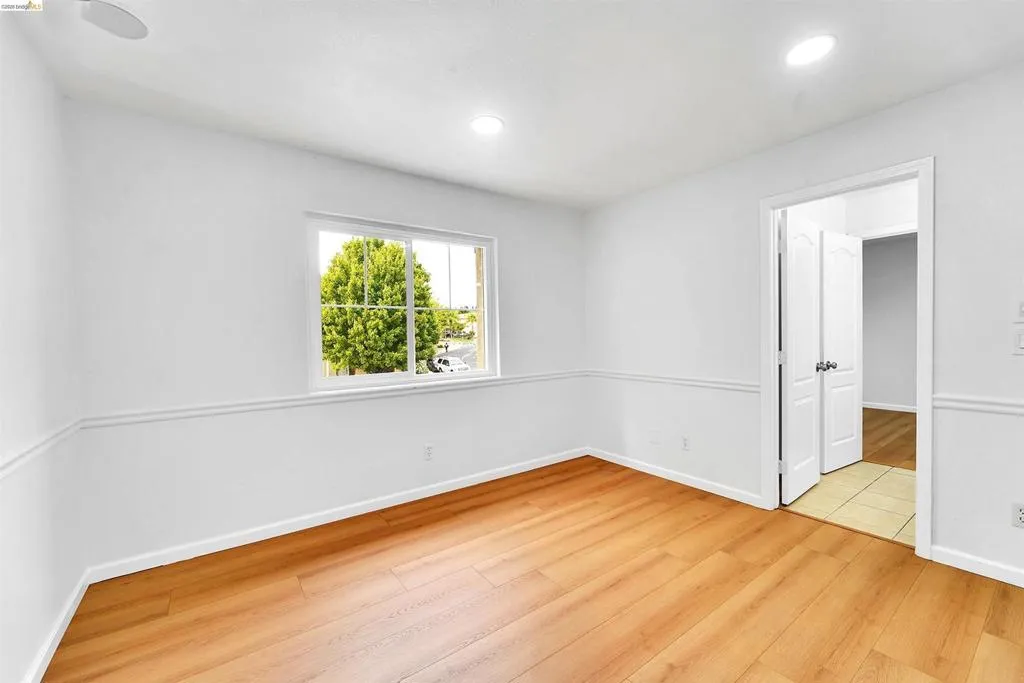 Room featuring wood-finish flooring, white walls with chair rail molding, and a window providing natural light