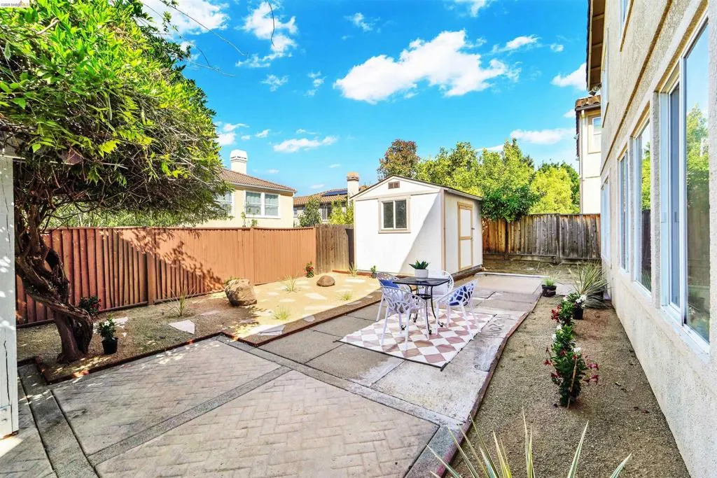Rear yard featuring a white storage shed, brick-patterned concrete patio, and perimeter fencing