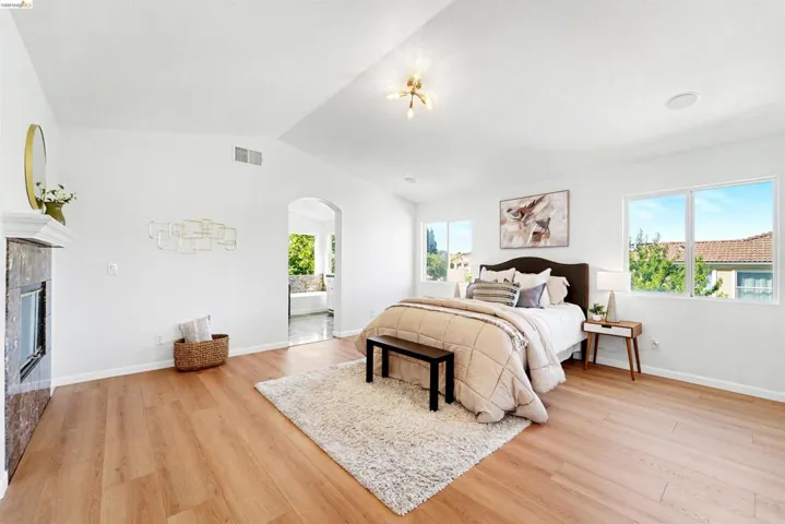 Spacious room featuring vaulted ceilings, light wood-finish flooring, a fireplace with a dark stone surround and white mantel, and an arched doorway