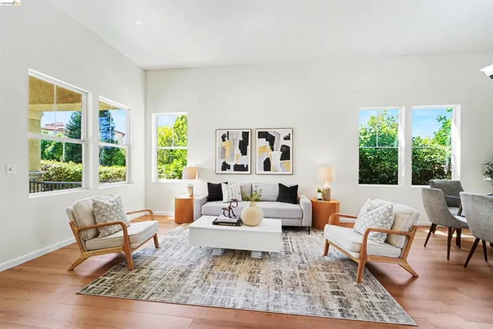 Spacious living area featuring light wood-finish flooring, abundant natural light from multiple windows, and a neutral color palette