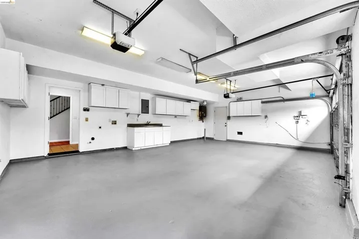 Spacious two-car garage featuring a painted concrete floor, built-in cabinetry, a utility sink, and overhead lighting