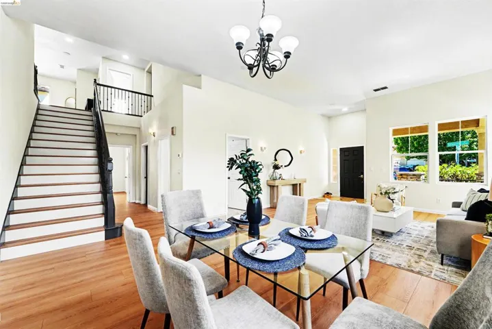 Open-concept living area with wood-finish flooring, a two-story staircase featuring dark wood newel posts and railings, and recessed lighting