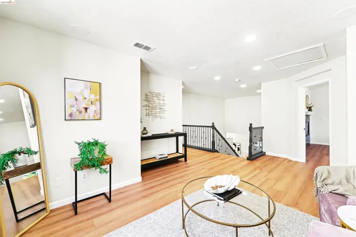 Spacious room featuring wood-finish flooring, recessed lighting, and a contemporary black wrought iron staircase railing