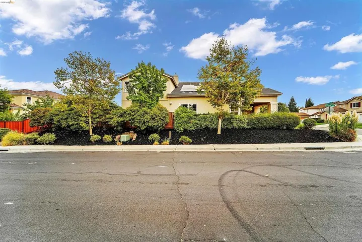 Property exterior featuring a stucco facade, mature landscaping with dark mulch, and a red perimeter fence