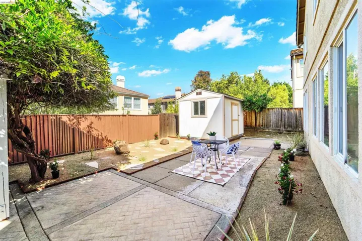 Rear yard featuring a white storage shed, brick-patterned concrete patio, and perimeter fencing