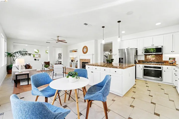 Open-concept kitchen and living area featuring white cabinetry, stainless steel appliances, a large central island with seating, and a fireplace with a mantel