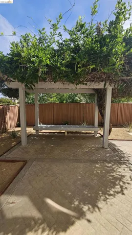Patio area featuring a pergola with mature greenery, an integrated bench, and patterned concrete flooring