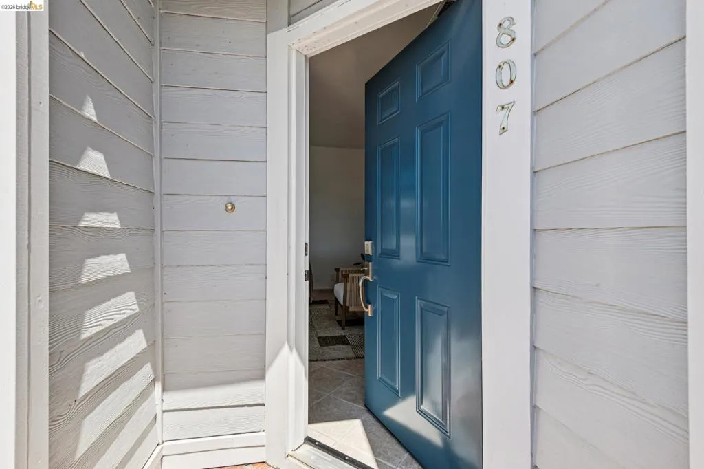 Entryway featuring a paneled teal door with polished hardware, white horizontal siding, and tiled flooring
