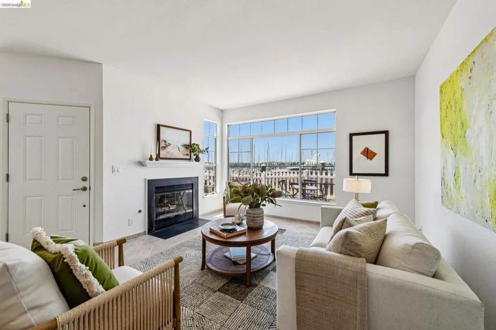 Living space featuring large windows overlooking a marina, a white paneled door, a fireplace with a black stone surround and white mantel, and light-colored flooring