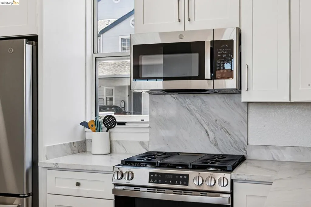 Stainless steel range and microwave oven with white shaker-style cabinetry, a white countertop, and a marble-patterned backsplash