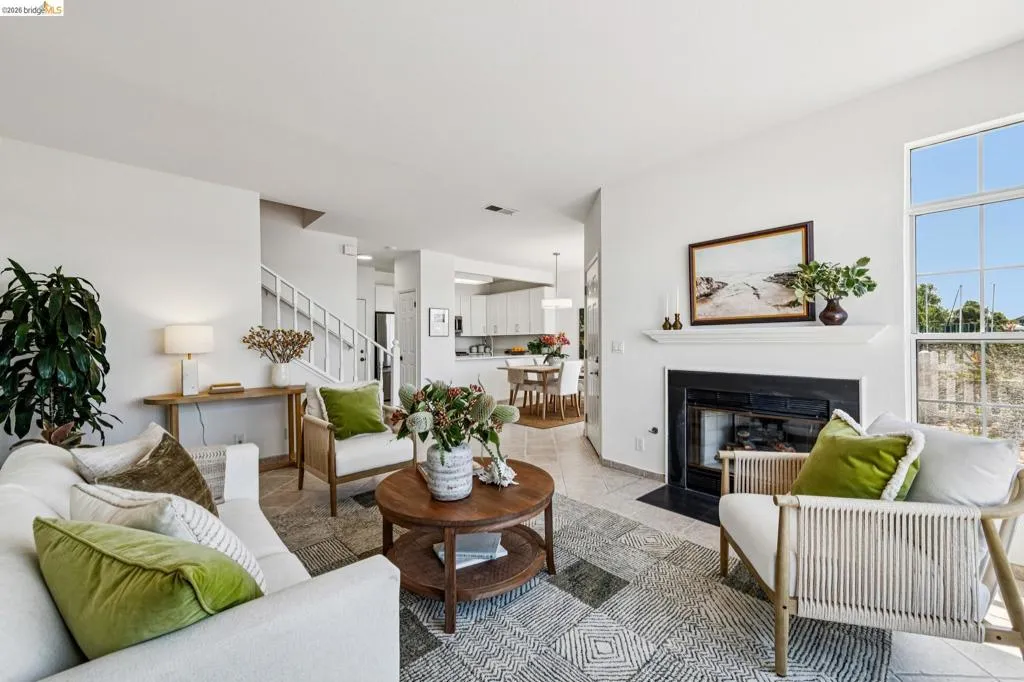 Living area featuring a fireplace with a black hearth and white mantel, a large window, tiled flooring, and a staircase with white railings