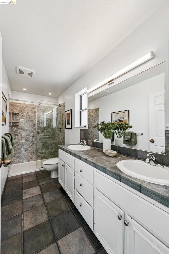 Bathroom featuring a double vanity with white cabinetry and dark tile countertop, dual undermount sinks, and a large wall-mounted mirror