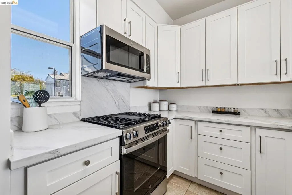 Modern kitchen featuring white shaker cabinetry, stainless steel appliances, marble-look countertops, and a matching backsplash